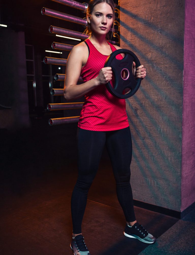 Girl athlete keeps the disc from the bar weighting agent for doing crossfit and fitness. Concept of sports equipment and weight loss.